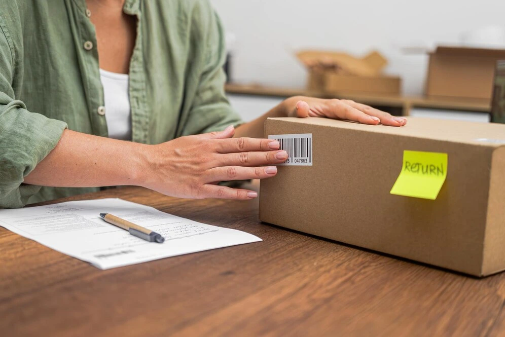 manos-consumidor-femenino-pegan-codigo-barras-caja-carton-pegatina-amarilla-palabra-retorno_210545-17684.webp